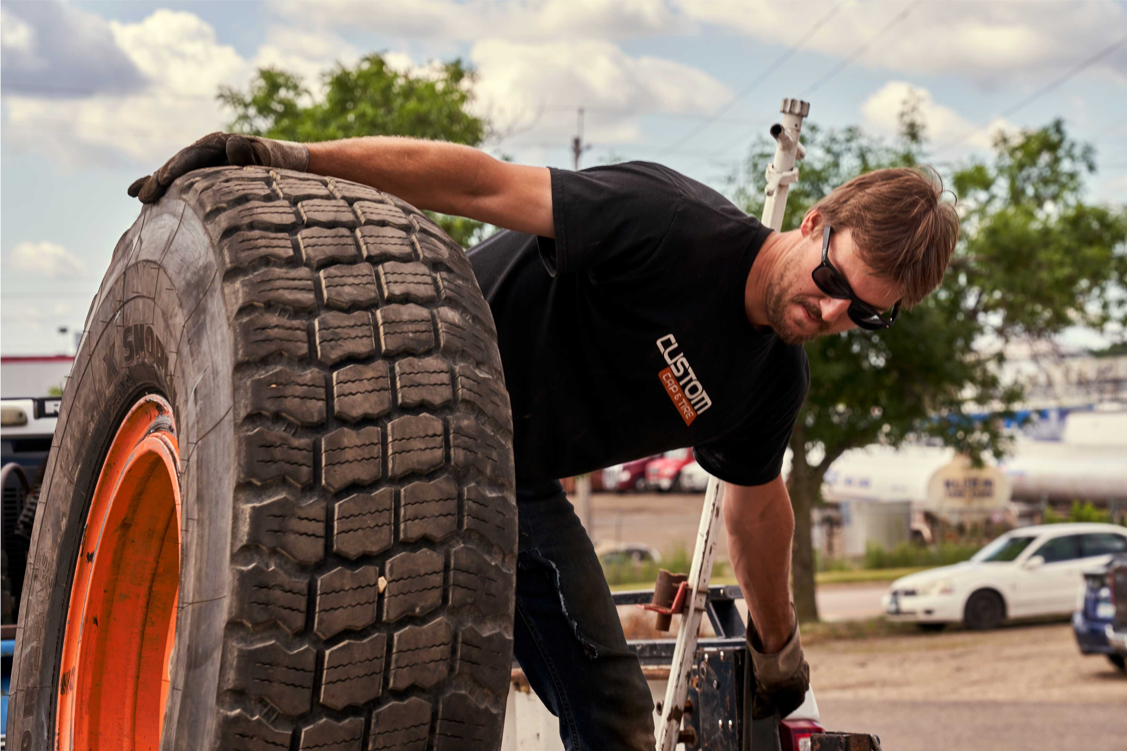 A Custom Cap and Tire employee wearing a branded t-shirt moves a tire.